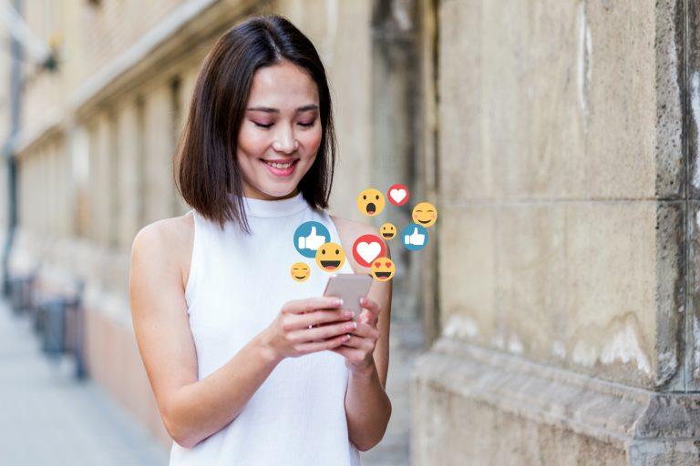 Mulher asiática mexendo no celular com emojis saindo
